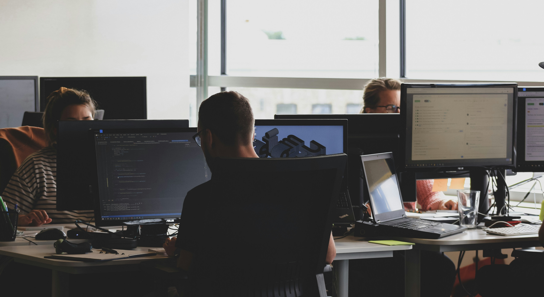 Individuals gathered in an office setting, using their personal desktops for a variety of digital tasks.